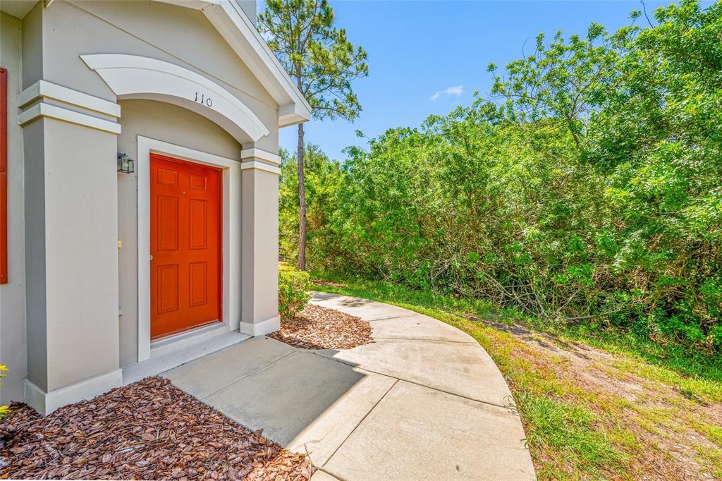 A concrete walkway leads to a house entrance with a bright orange front door — 10409 CRIMSON PARK LANE UNIT 110, TAMPA, FL