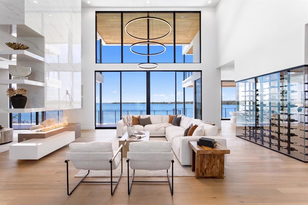 A modern living room features a fireplace, floor-to-ceiling windows, and a glass-enclosed wine cellar — 114 SANDS POINT DRIVE, TIERRA VERDE, FL