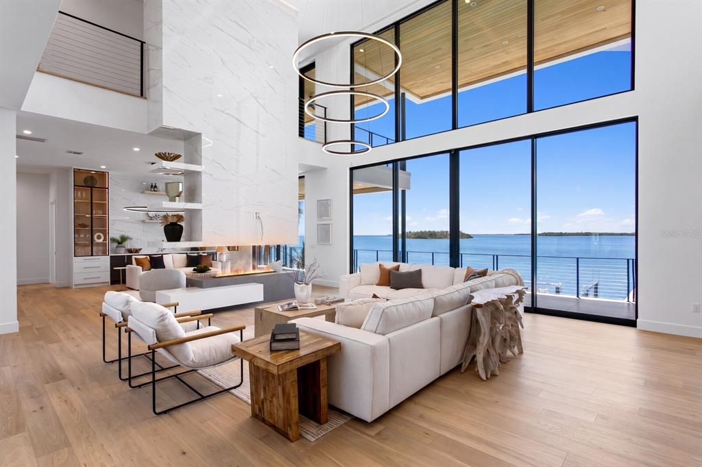 A modern living room features a marble fireplace, floor-to-ceiling windows, and a waterfront view — 114 SANDS POINT DRIVE, TIERRA VERDE, FL
