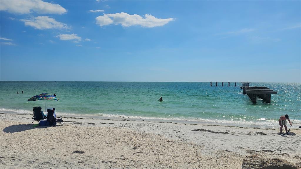 A sandy beach with a pier, a beach umbrella, and people enjoying the water — 13073 PROCTOR AVENUE, PORT CHARLOTTE, FL