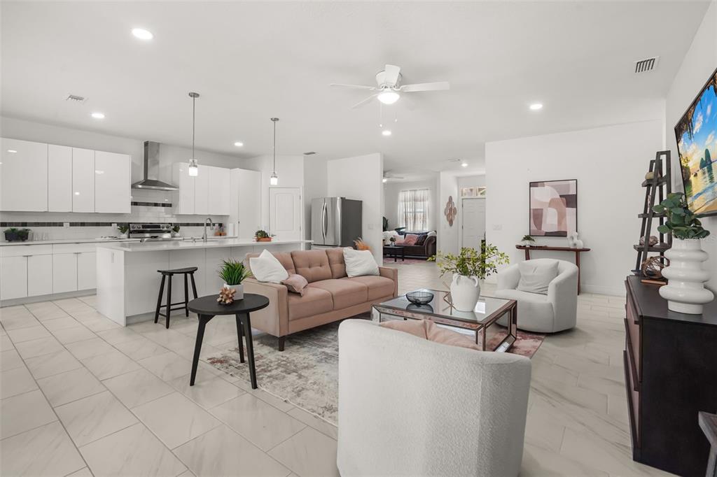An open-concept living room and kitchen featuring white cabinetry, a pink sofa, and tile flooring — 16626 BEARLE ROAD, ORLANDO, FL
