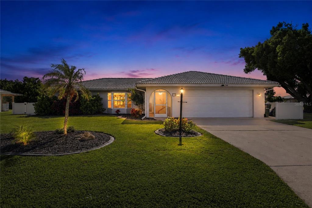 A single-story house with a white garage, arched entryway, and palm tree at dusk — 302 DEGAS DRIVE, NOKOMIS, FL