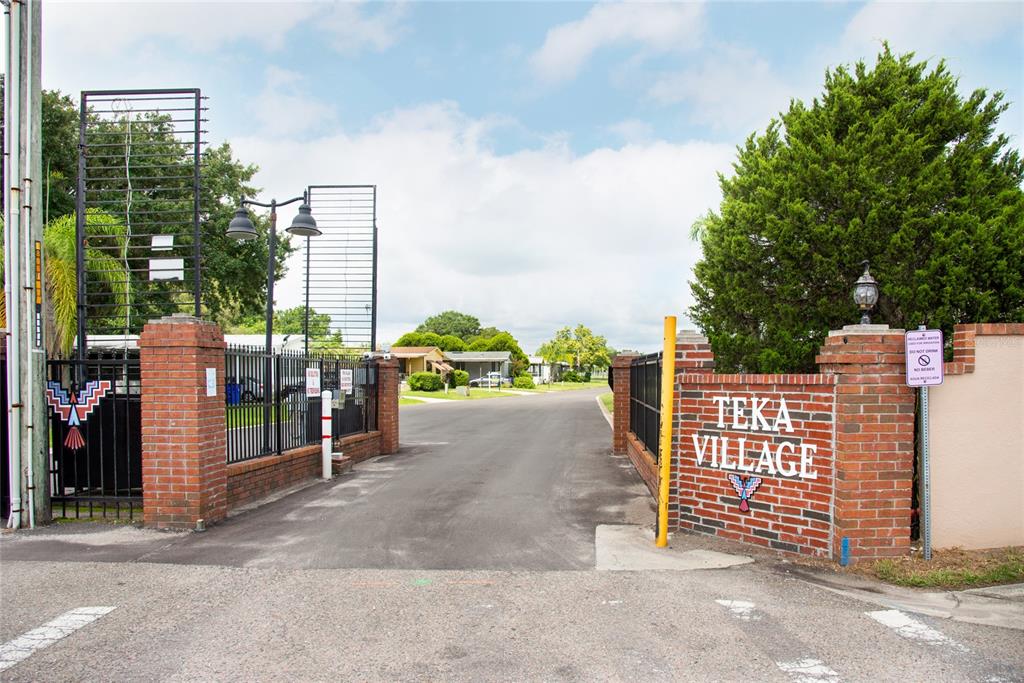 The entrance to Teka Village features a brick gate with metal fencing and signage — 2542 LONGPINE LANE, ST CLOUD, FL