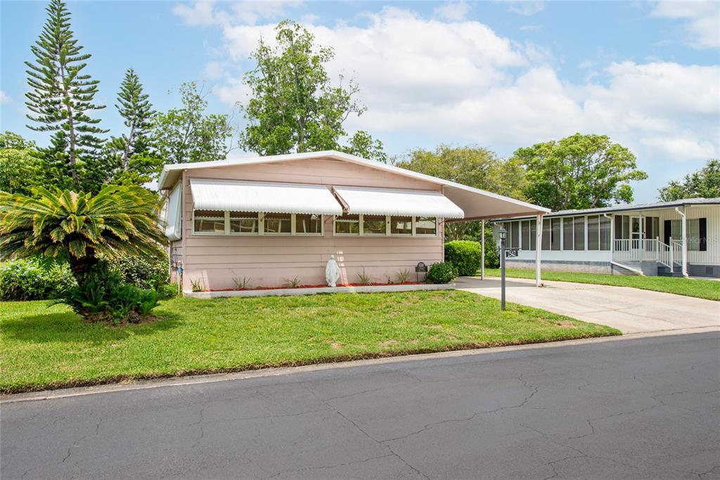 A light pink mobile home with a carport and white awnings sits on a lawn — 2542 LONGPINE LANE, ST CLOUD, FL
