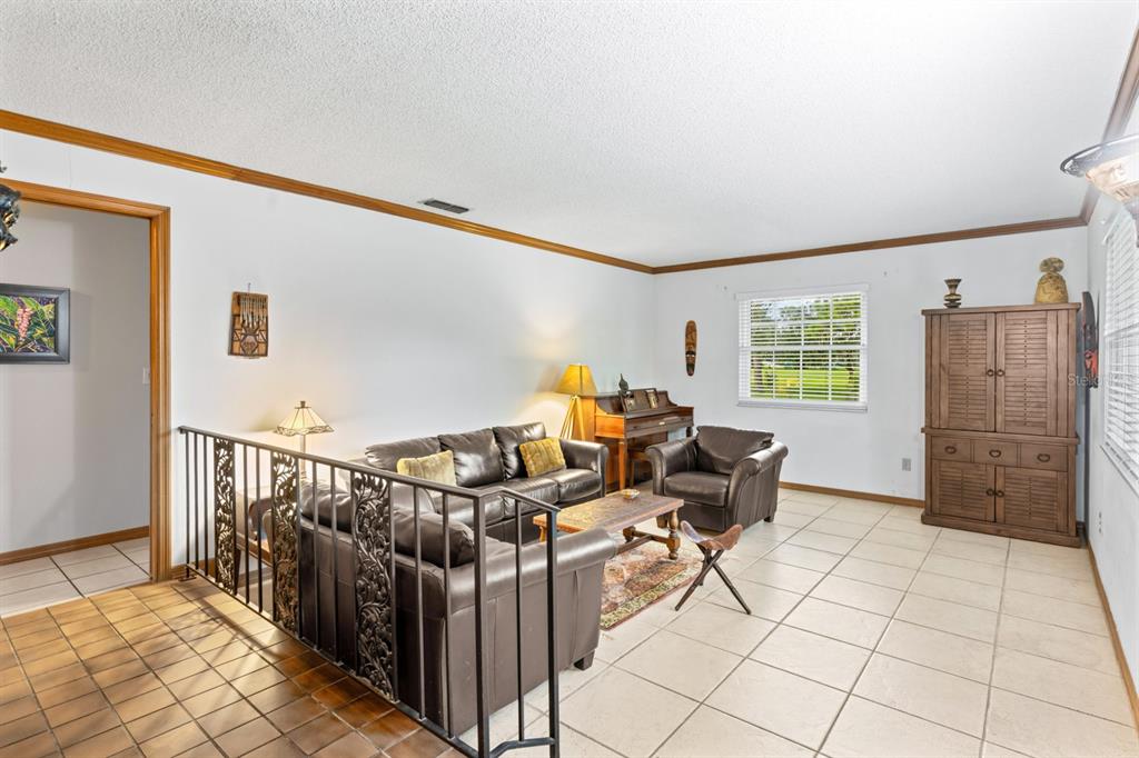 A living room features tile flooring, a leather sofa set, a piano, and a metal railing — 116 BEAUFORT DRIVE, LONGWOOD, FL