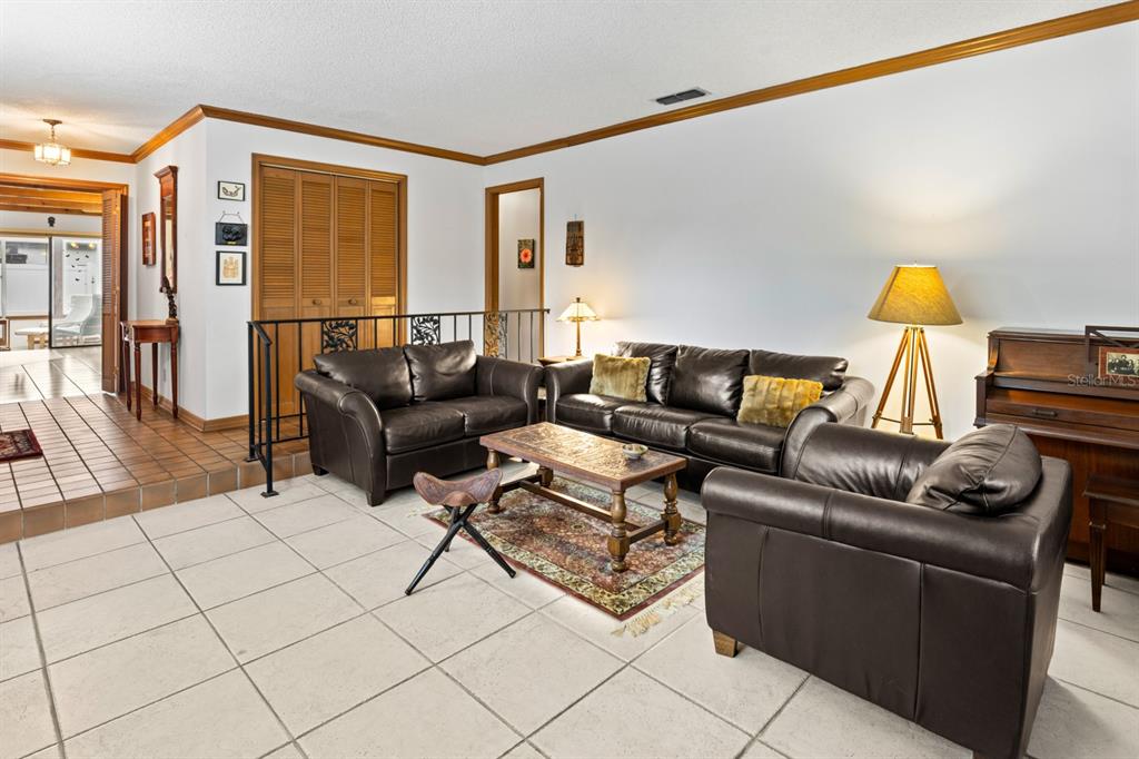 A living room features tiled floors, dark leather furniture, a coffee table, and a piano — 116 BEAUFORT DRIVE, LONGWOOD, FL