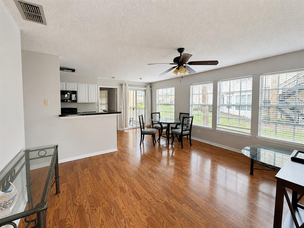 An open-concept living and dining area features wood-look flooring, a ceiling fan, and large windows — 1057 S HIAWASSEE ROAD UNIT 1918, ORLANDO, FL