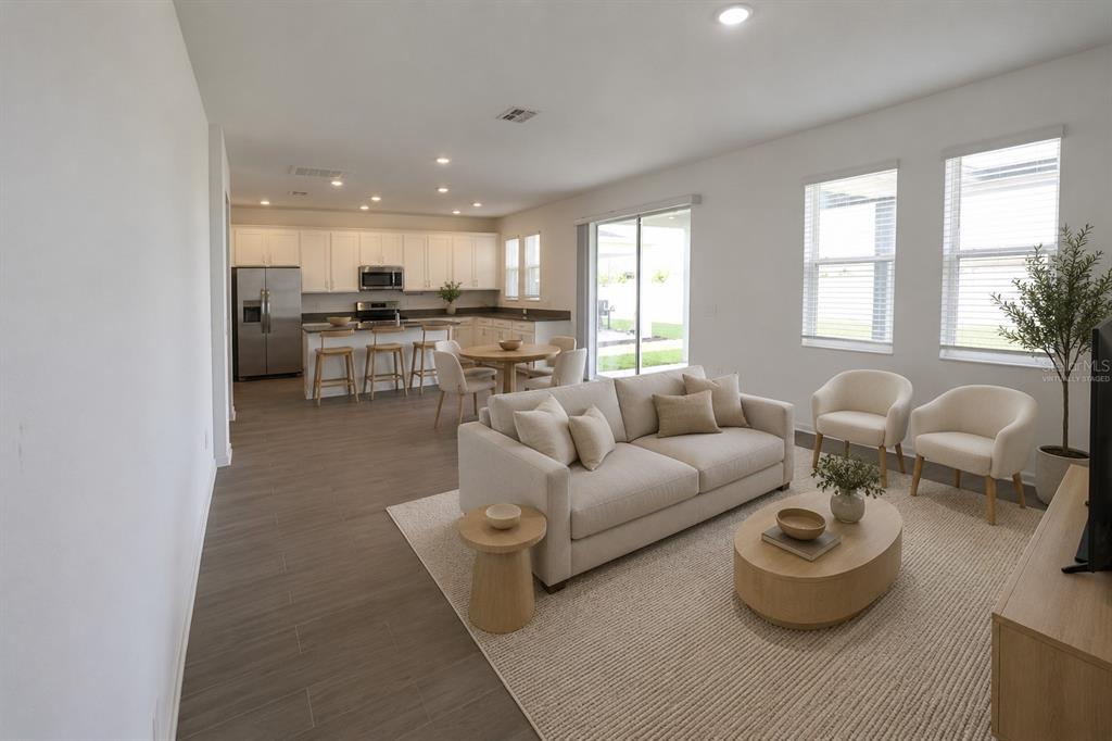 An open-concept living room and kitchen with light-colored furniture, white cabinets, and wood-look tile flooring — 2587 RUNNERS CIRCLE, CLERMONT, FL