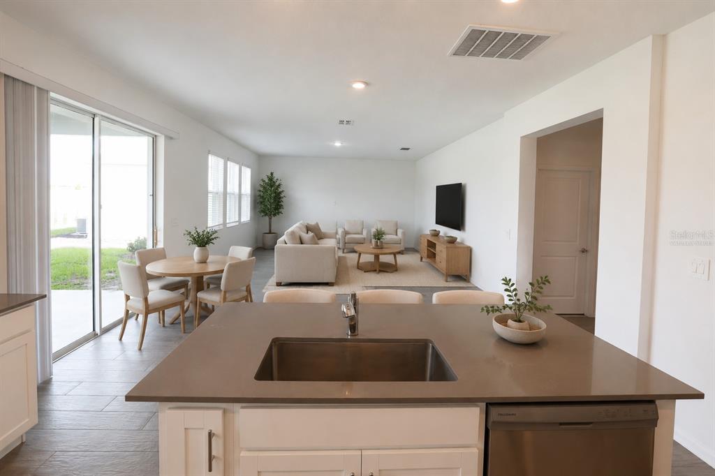 A kitchen island with a sink overlooks an open-concept living and dining area — 2587 RUNNERS CIRCLE, CLERMONT, FL