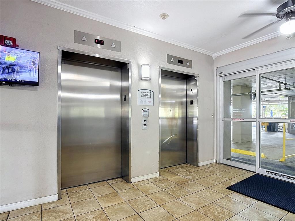 An indoor elevator lobby features two stainless steel elevator doors, tiled flooring, and glass sliding doors — 13427 BLUE HERON BEACH DRIVE UNIT 402, ORLANDO, FL