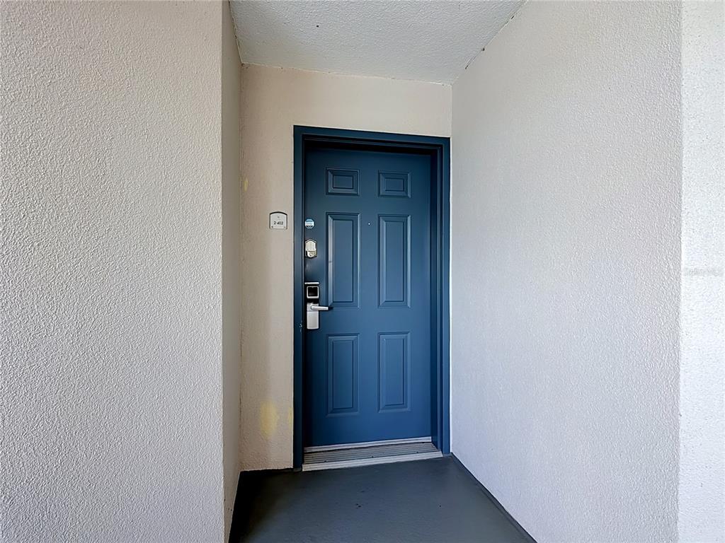 A blue front door with a digital lock is set within a white stucco entryway — 13427 BLUE HERON BEACH DRIVE UNIT 402, ORLANDO, FL