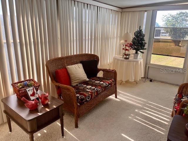 A sunroom features a wicker loveseat, a side table with decor, and vertical blinds — 3405 LANARK DRIVE, HOLIDAY, FL