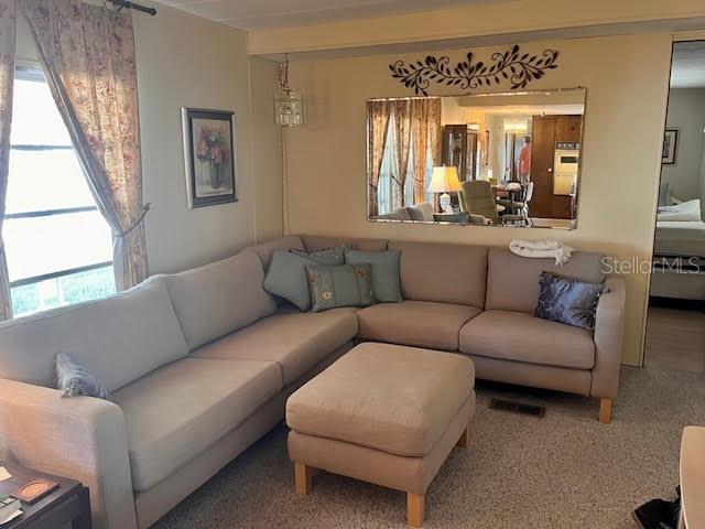 A living room features a large beige sectional sofa, a matching ottoman, and a wall mirror — 3405 LANARK DRIVE, HOLIDAY, FL
