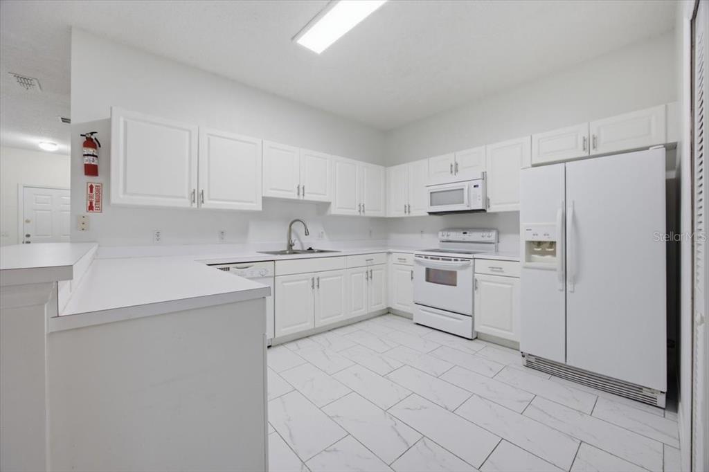 A white kitchen features white cabinets, matching appliances, and light-colored tile flooring — 3166 SUN LAKE COURT UNIT B, KISSIMMEE, FL