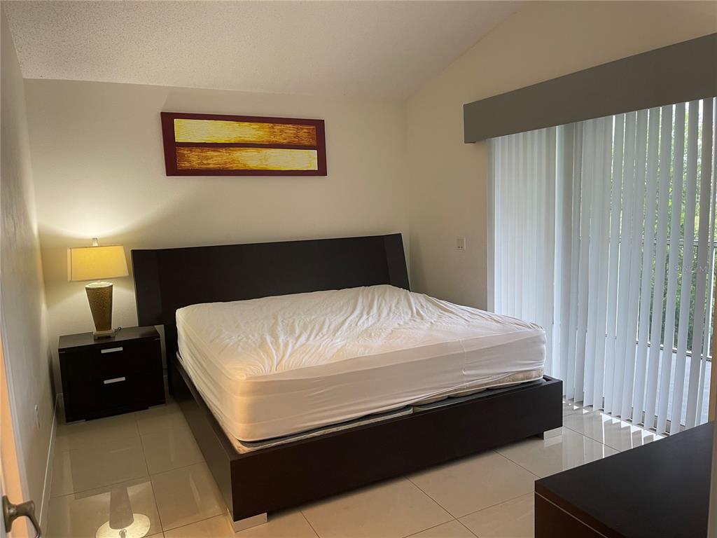 A bedroom features a dark wood bed frame, a matching nightstand, and white tile flooring — 3166 SUN LAKE COURT UNIT B, KISSIMMEE, FL