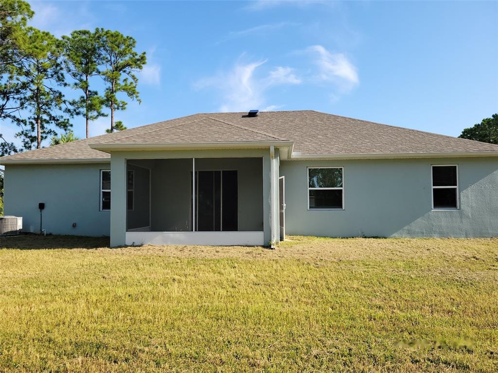 The rear exterior of a single-story house features a screened-in porch and a grassy yard — 780 CONSUMER STREET SE, PALM BAY, FL