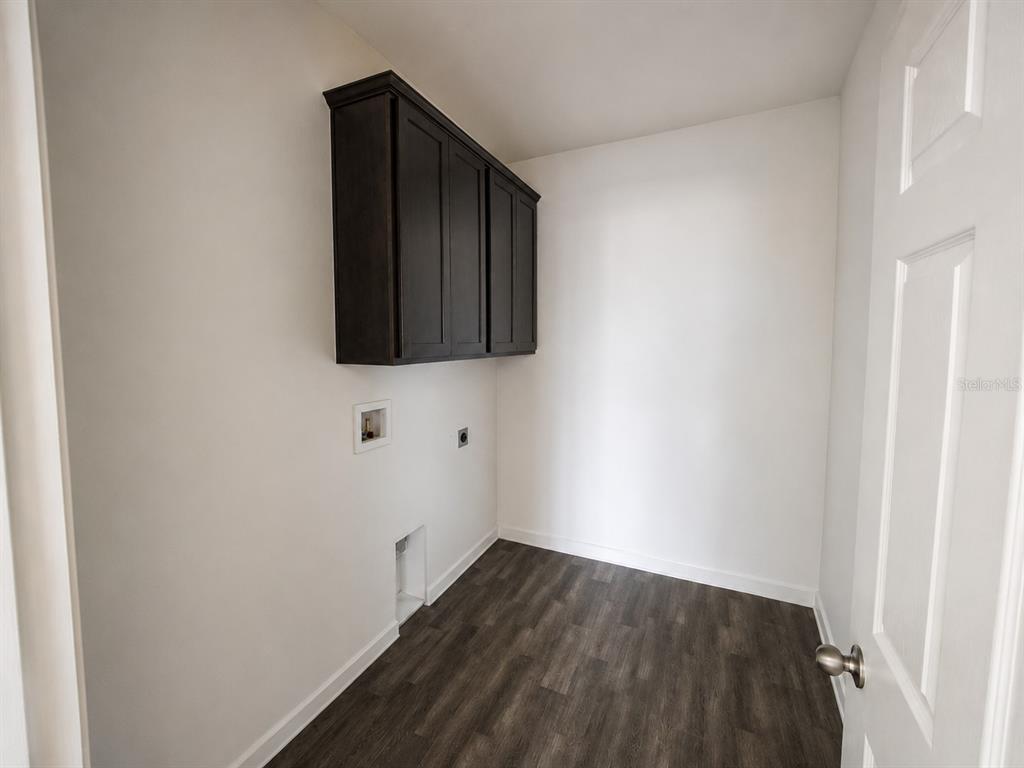 A laundry room with dark wood cabinets, white walls, and wood-look flooring — 780 CONSUMER STREET SE, PALM BAY, FL