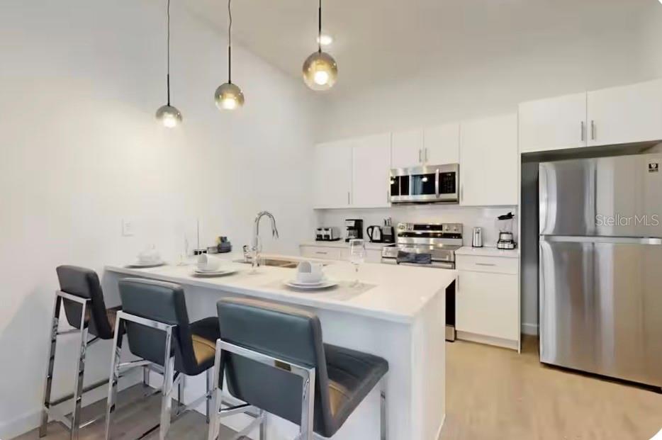 A modern kitchen features white cabinets, stainless steel appliances, and a breakfast bar with three chairs — 613 TRIKOMO DRIVE, DAVENPORT, FL