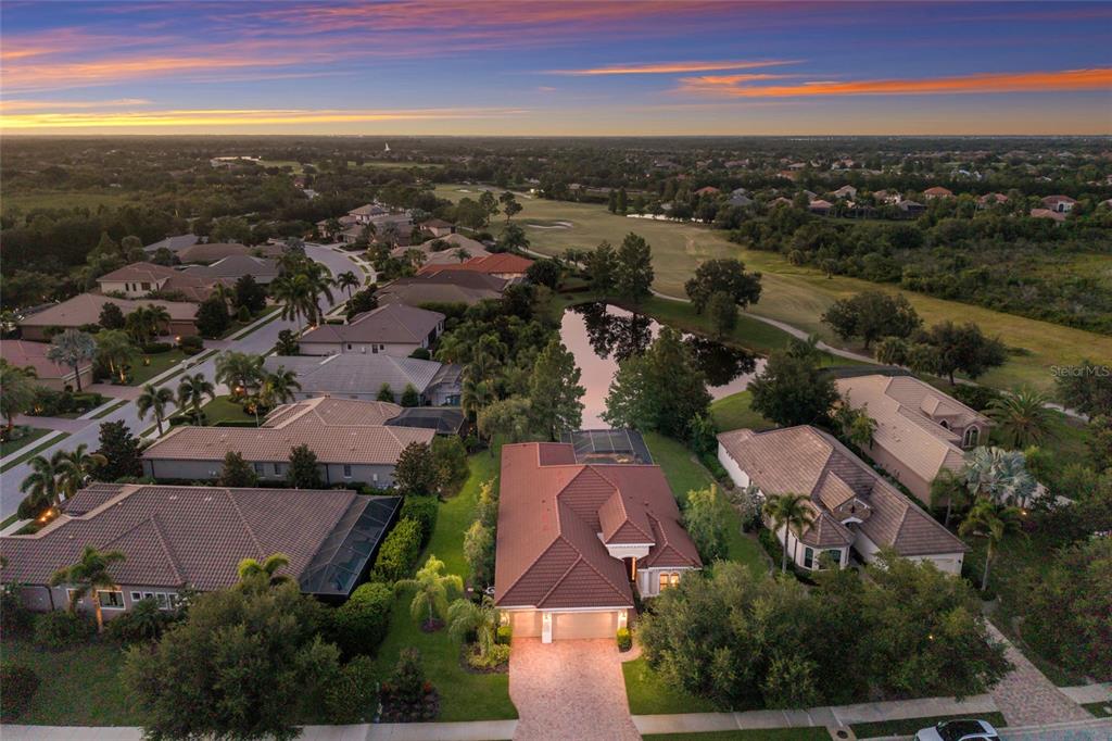 An aerial view of a suburban neighborhood featuring houses with tiled roofs and a central pond — 15403 HELMSDALE PLACE, LAKEWOOD RANCH, FL