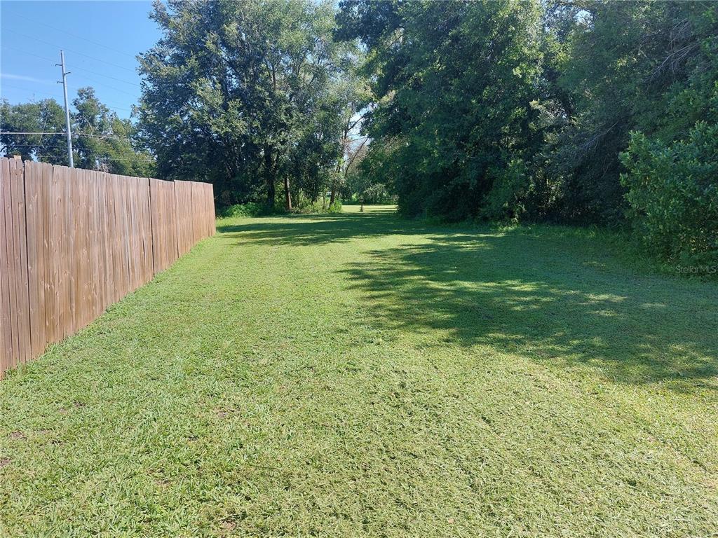 A grassy, rectangular lot is bordered by a wooden fence on the left and trees — WALDO, DADE CITY, FL