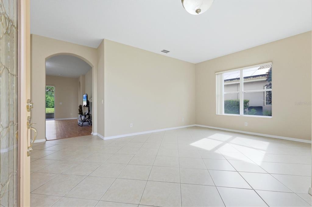 A bright, empty room features beige walls, light-colored tile flooring, and an arched entryway — 4612 62ND AVENUE E, BRADENTON, FL