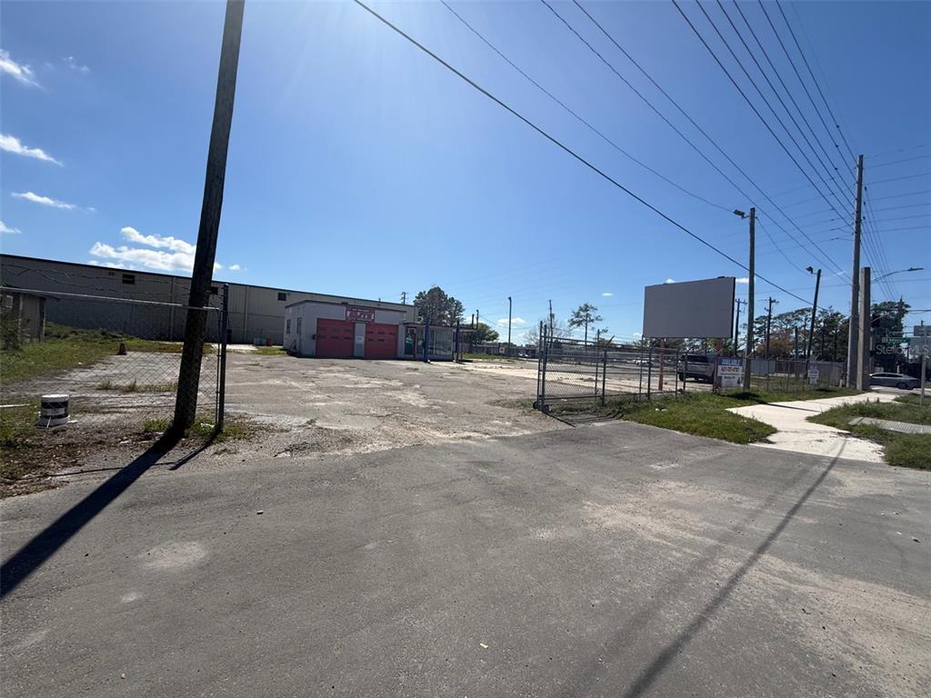 A fenced commercial lot features a small building with red garage doors under blue skies — 3960 SILVER STAR ROAD, ORLANDO, FL