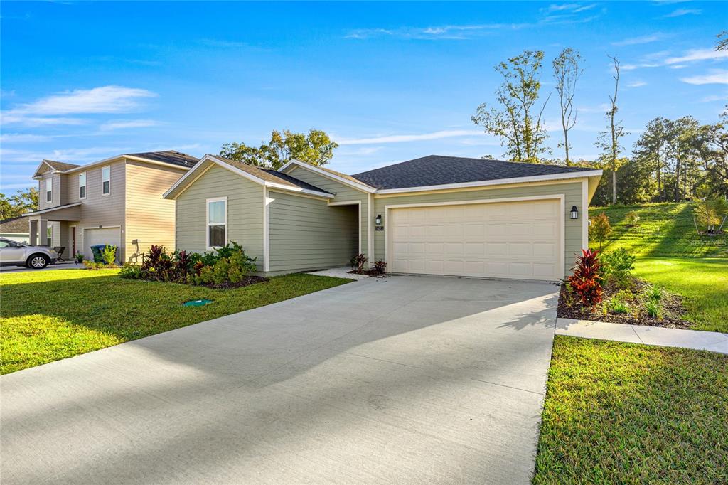 A single-story house with light green siding and a two-car garage under a blue sky — 16927 NW 144TH STREET, ALACHUA, FL