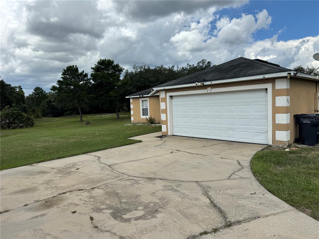 A beige house with a white garage door and a cracked concrete driveway — 609 KISSIMMEE LANE, POINCIANA, FL