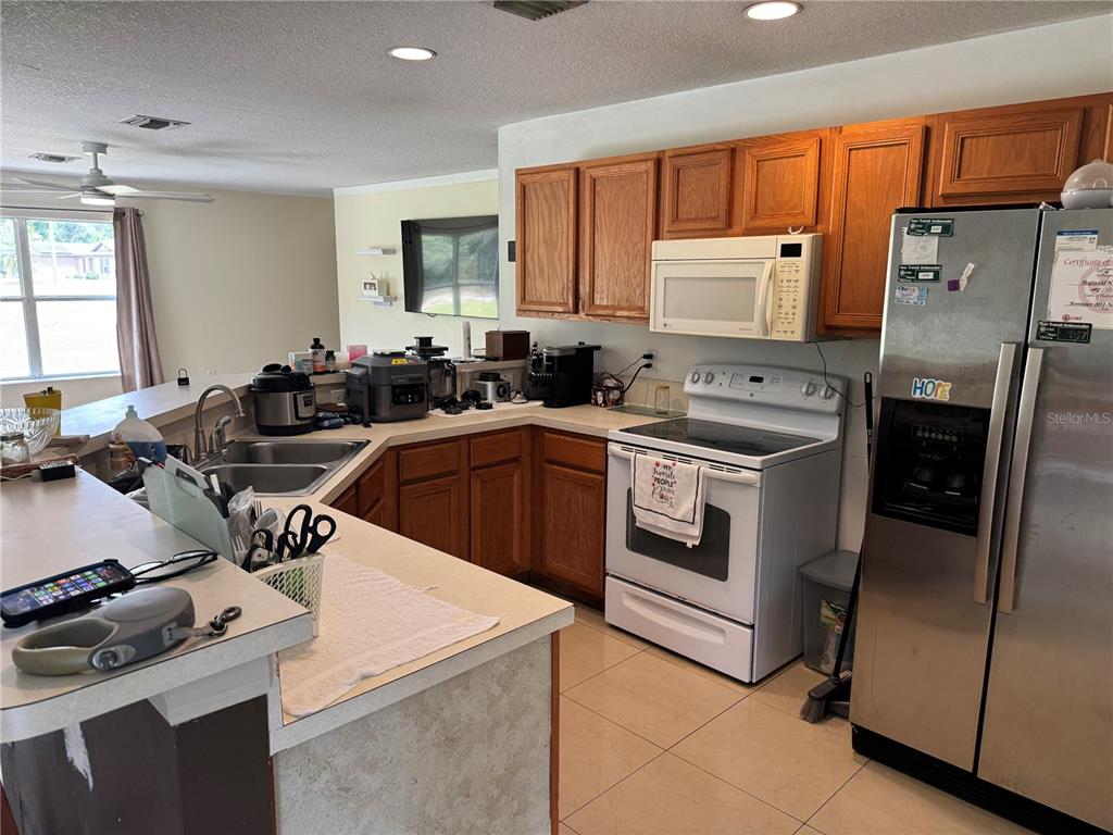 A kitchen features wood cabinets, white appliances, a stainless steel refrigerator, and a breakfast bar — 609 KISSIMMEE LANE, POINCIANA, FL
