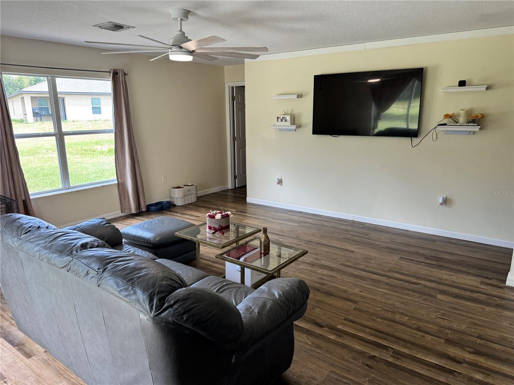 A living room features wood-look flooring, a gray leather sofa, a ceiling fan, and a television — 609 KISSIMMEE LANE, POINCIANA, FL
