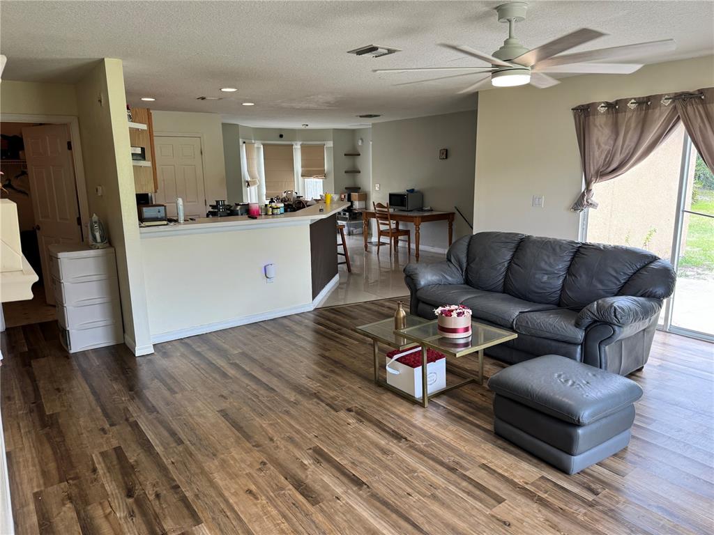 A living room with wood-look flooring, a gray leather sofa, and an open kitchen area — 609 KISSIMMEE LANE, POINCIANA, FL