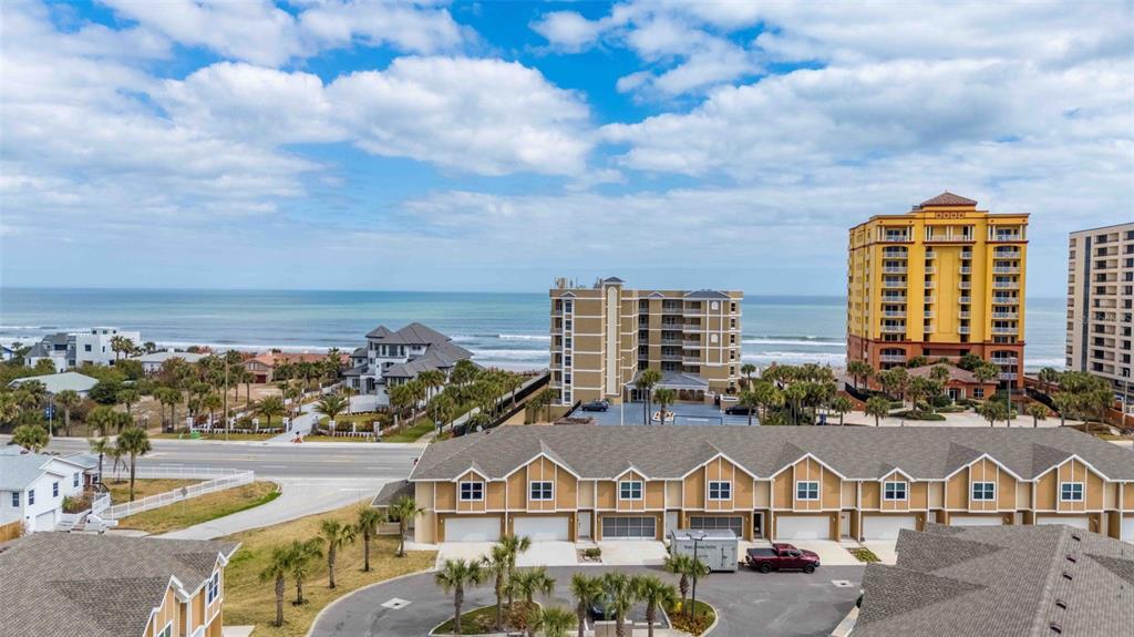 An aerial view shows a tan townhouse complex with a parking lot and nearby high-rises — 108 OCEANS CIRCLE, DAYTONA BEACH, FL
