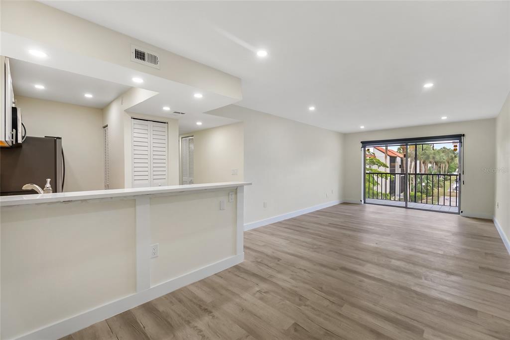 An open-concept living area features light wood-look flooring, a kitchen breakfast bar, and a balcony — 3229 BENEVA ROAD UNIT 203, SARASOTA, FL