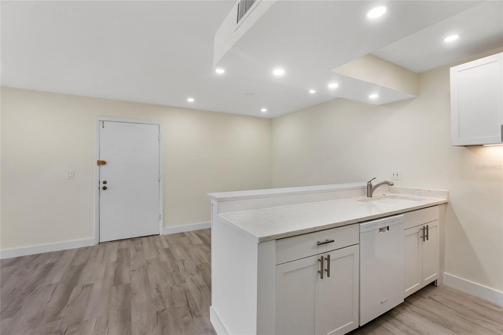 A kitchen with white cabinets and a peninsula overlooks an open living area with wood-look flooring — 3229 BENEVA ROAD UNIT 203, SARASOTA, FL