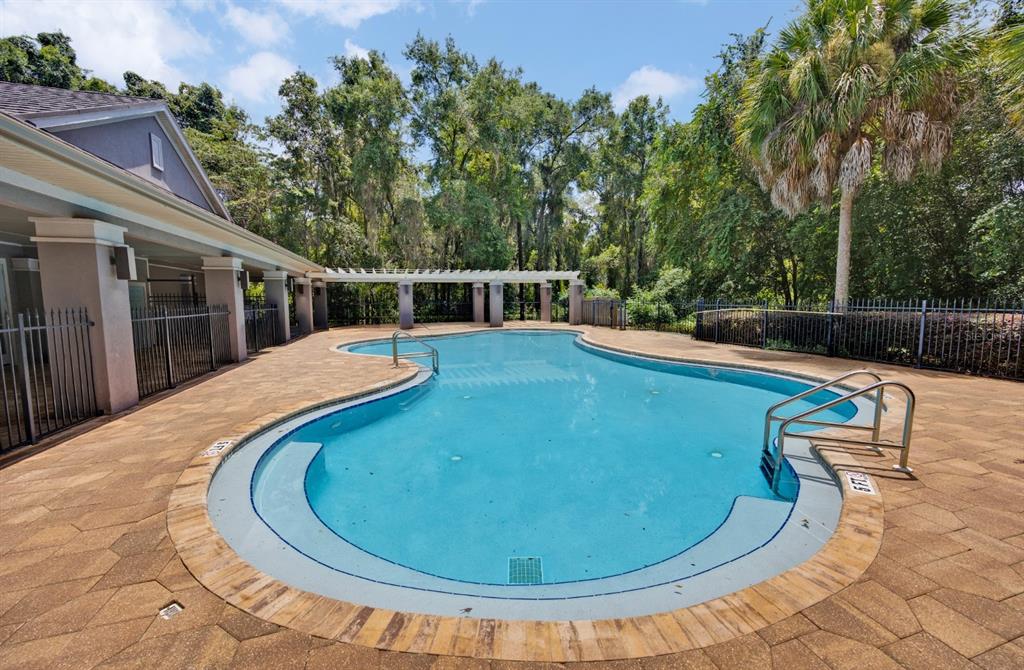 An outdoor swimming pool with a paved deck, metal fencing, and a pergola in the background — 13639 NW 13TH PLACE, NEWBERRY, FL