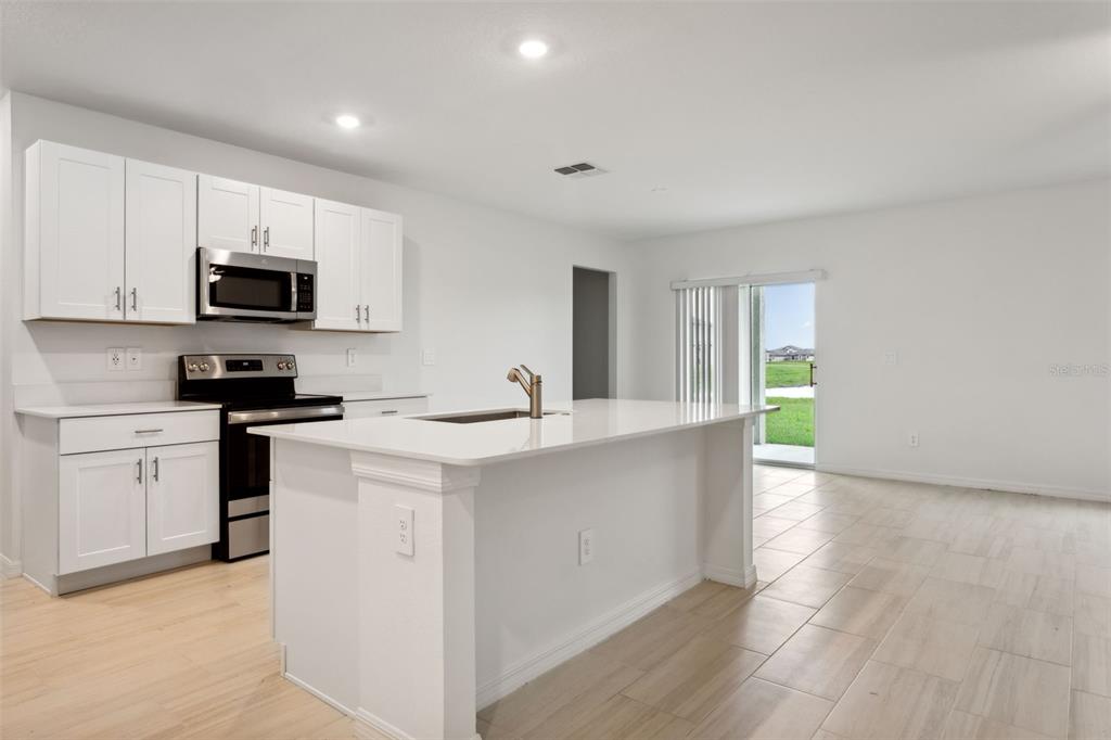 A modern kitchen features white cabinets, stainless steel appliances, a center island, and tile flooring — 32309 WISHING HAVEN DRIVE, SAN ANTONIO, FL