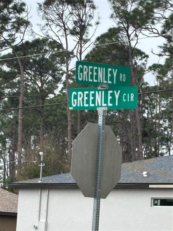 A street sign shows the intersection of Greenley Road and Greenley Circle against a wooded background — GREENLEY CIRCLE, NORTH PORT, FL
