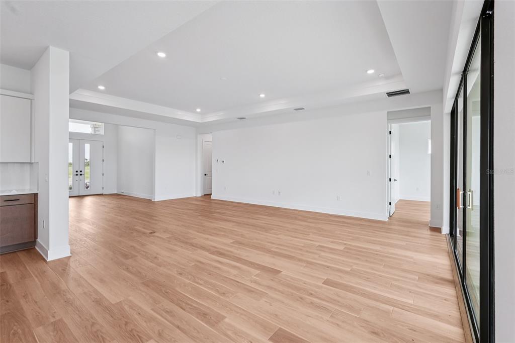 A spacious, minimalist living area features light wood flooring, white walls, and a tray ceiling — 12652 IVORY TUSK LANE, SPRING HILL, FL