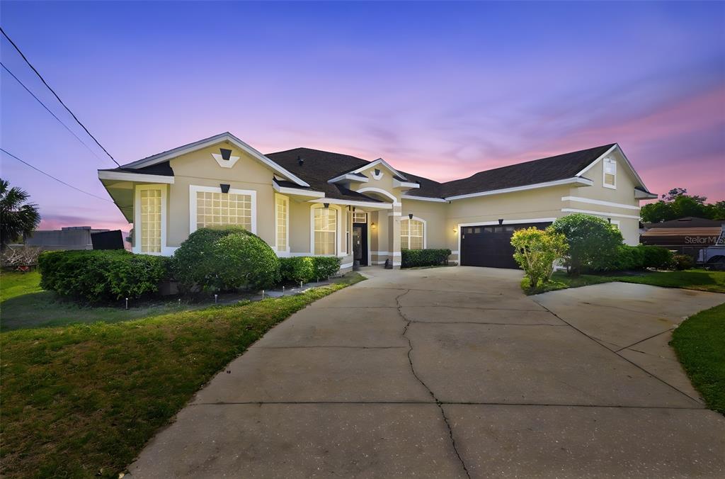 A single-story house with a beige exterior, a dark roof, and a concrete driveway at dusk — 1051 DUNBAR AVENUE, SANFORD, FL