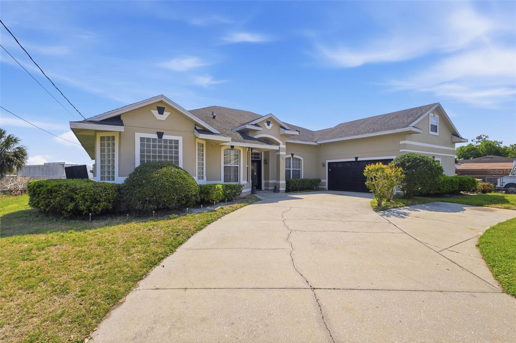 A tan single-story house with a concrete driveway and a dark two-car garage — 1051 DUNBAR AVENUE, SANFORD, FL