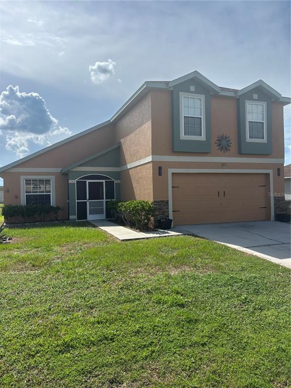 A two-story house with a tan stucco exterior, a two-car garage, and a screened entryway — 664 BROCKTON DRIVE, KISSIMMEE, FL