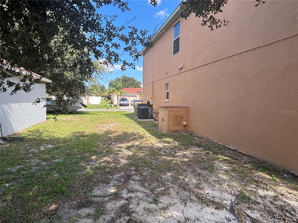 The side yard of a house features a tan stucco wall, an air conditioning unit, and landscaping — 664 BROCKTON DRIVE, KISSIMMEE, FL