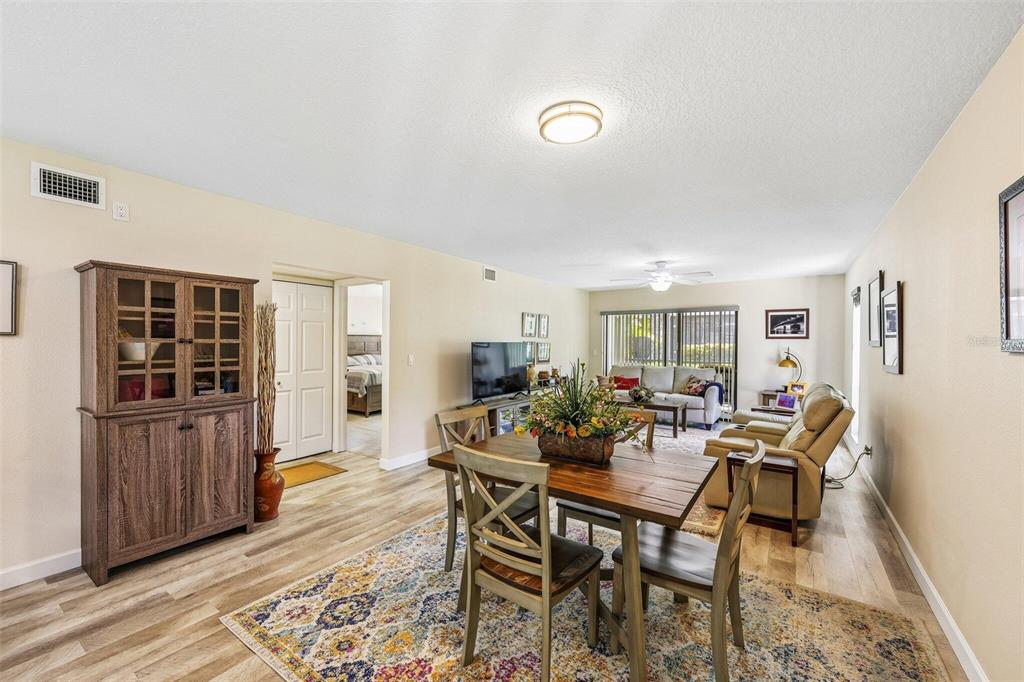 A dining area with a wooden table and chairs sits in an open-concept living room — 5400 34TH STREET W UNIT A6, BRADENTON, FL