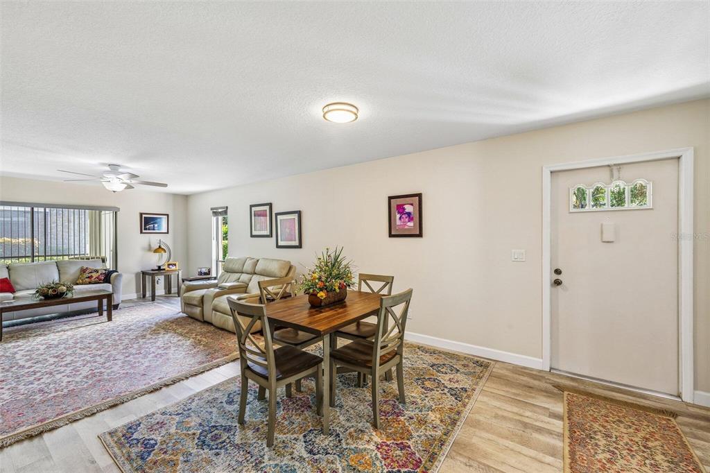An open-concept living and dining area features light wood flooring, neutral walls, and area rugs — 5400 34TH STREET W UNIT A6, BRADENTON, FL