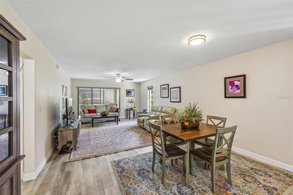 A living and dining room area with wood-look flooring, two area rugs, and neutral walls — 5400 34TH STREET W UNIT A6, BRADENTON, FL
