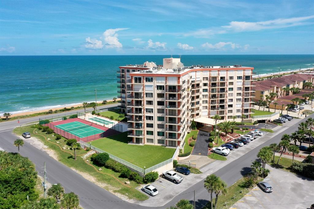 An aerial view shows a multi-story beachfront apartment building with a tennis court and parking — 3600 S OCEAN SHORE BOULEVARD UNIT 214, FLAGLER BEACH, FL