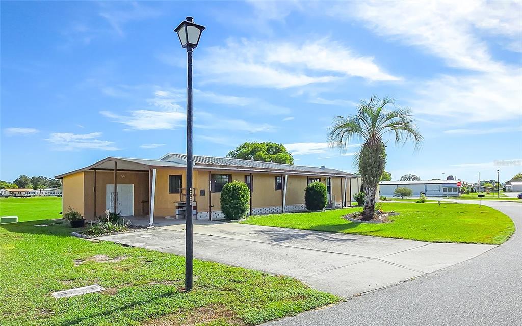 A single-story tan house with a carport and a palm tree sits on a lawn — 36301 CORONET WAY, ZEPHYRHILLS, FL