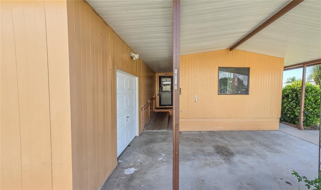 A covered carport leads to a white door and a ramped entrance to the home — 36301 CORONET WAY, ZEPHYRHILLS, FL