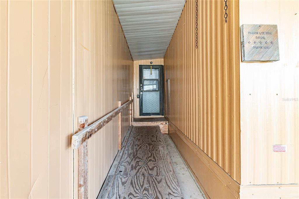 A narrow covered walkway leads to a glass-paneled door with a wooden ramp and railing — 36301 CORONET WAY, ZEPHYRHILLS, FL
