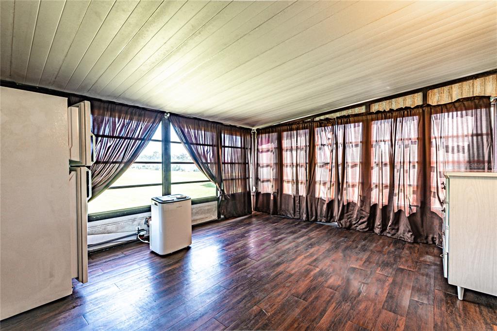 A sunroom with wood-look flooring, a portable air conditioner, and large windows with brown curtains — 36301 CORONET WAY, ZEPHYRHILLS, FL